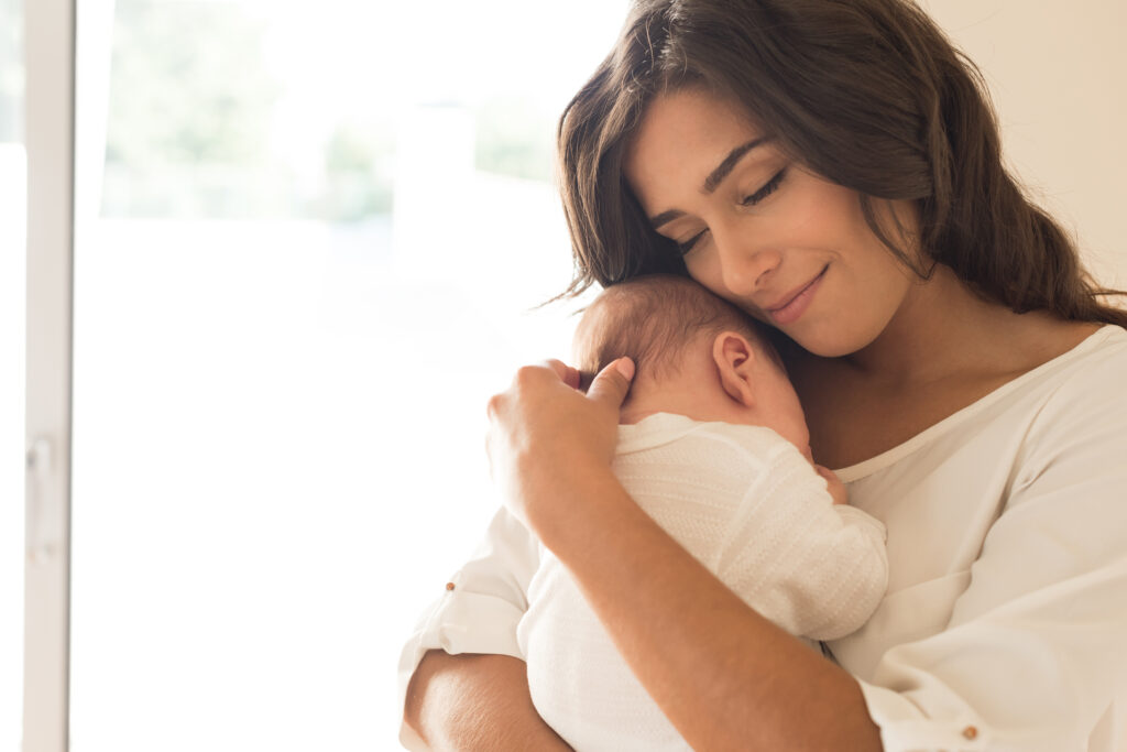 Woman seen from the front closing her eyes and cuddling her baby