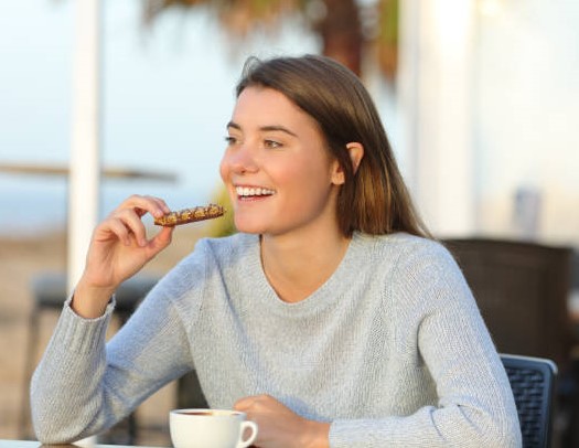 Young woman eating her cereal bar sitting by the sea