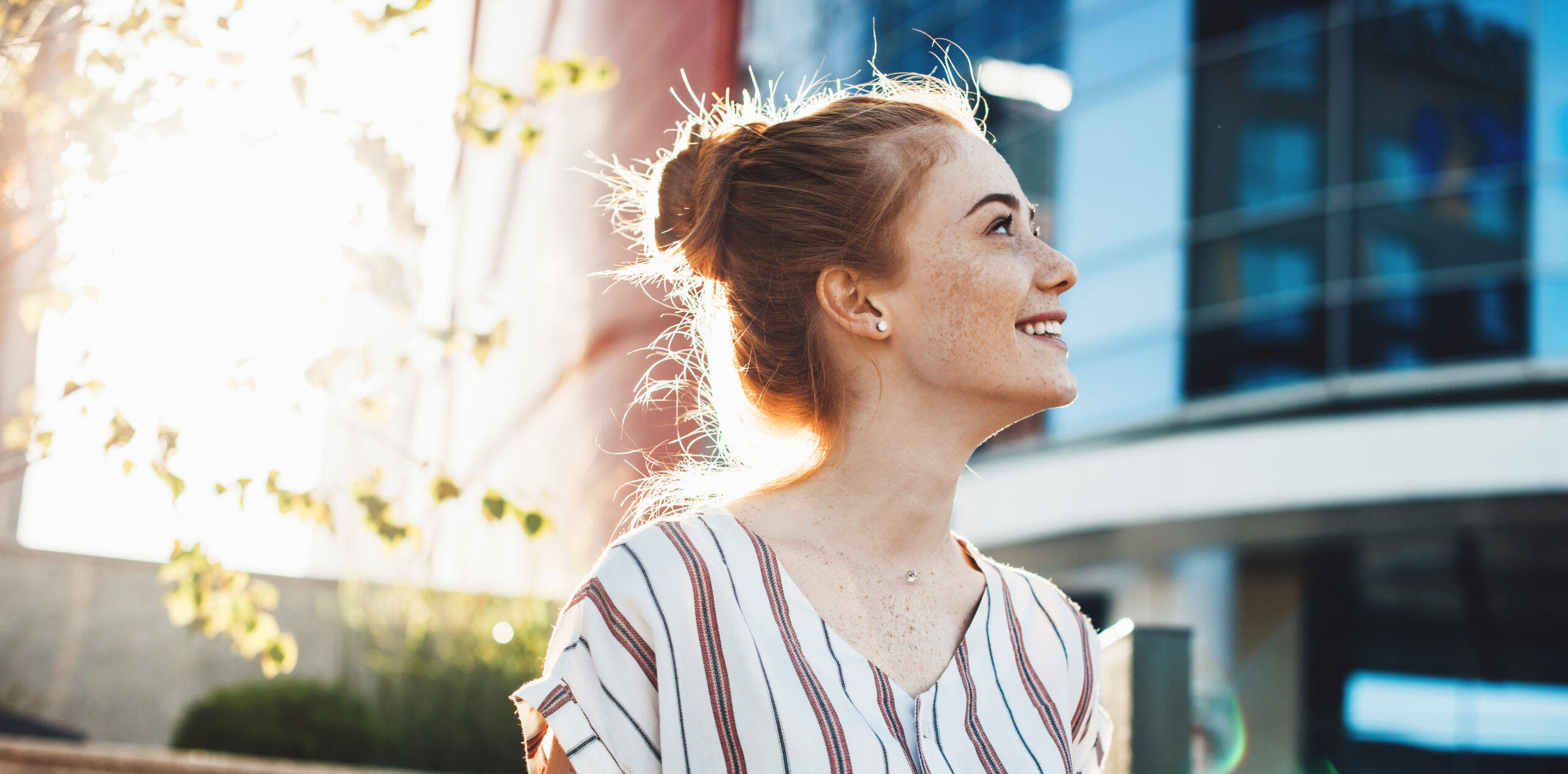 Cheerful young woman with freckles and red hair posing against the sunshine and smile looking up