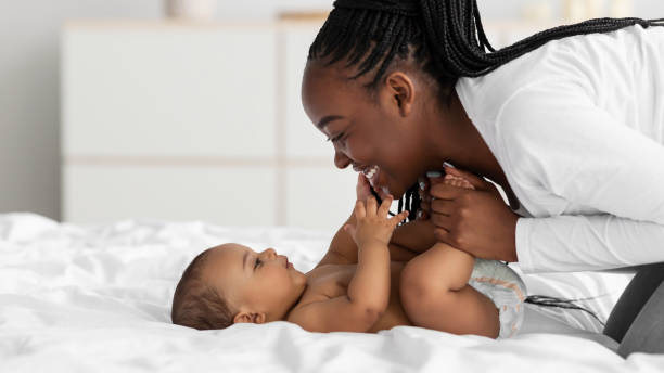Close-up profile portrait of a young black woman playing with her baby by holding her legs.