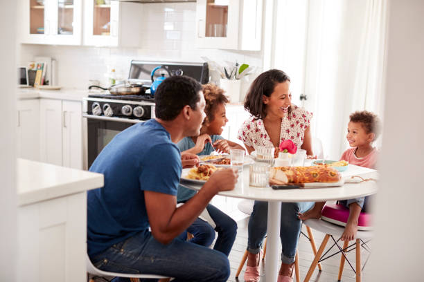 Un couple avec leur 2 enfants assis à la table de leur cuisine prenant leur repas, vue de l'embrasure de la porte.